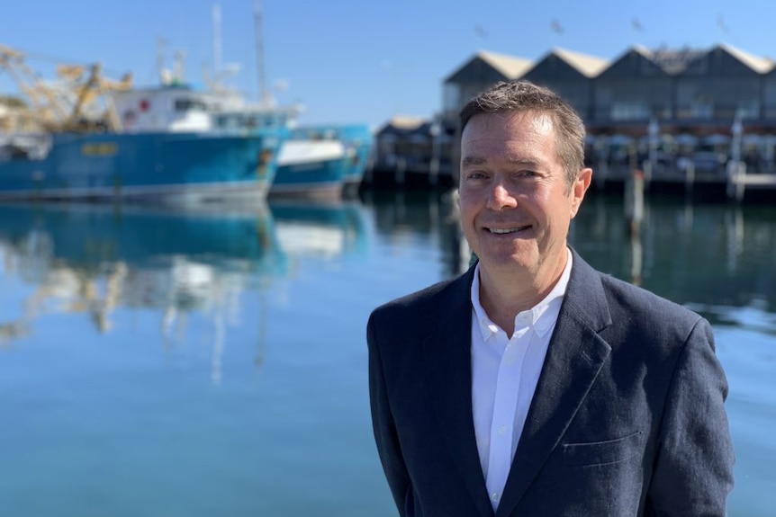 A portrait photo of Alex Ogg standing in front of a marina.