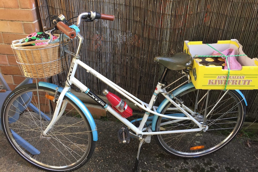 A bicycle with items in front basket and box containing baked goods strapped to pannier rack.