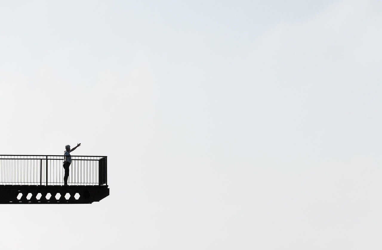 bw picture from far away of the side-on of a woman on a balcony, against blank sky