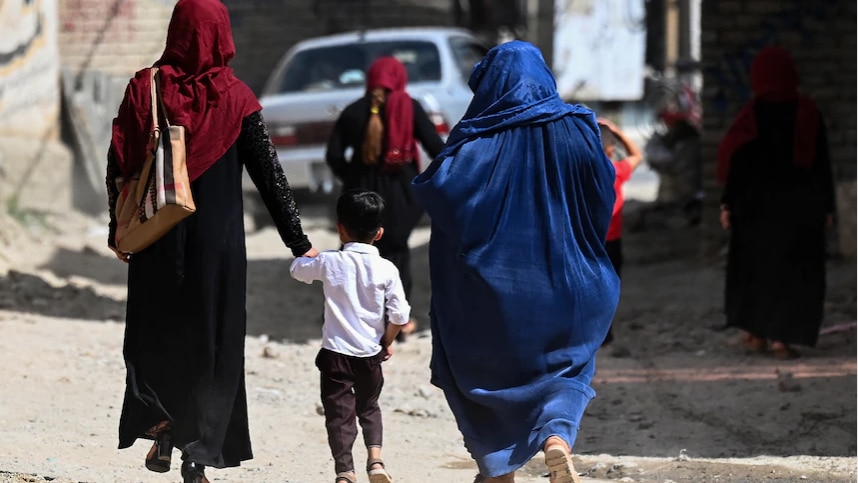 Two women walk with a child down a dusty road