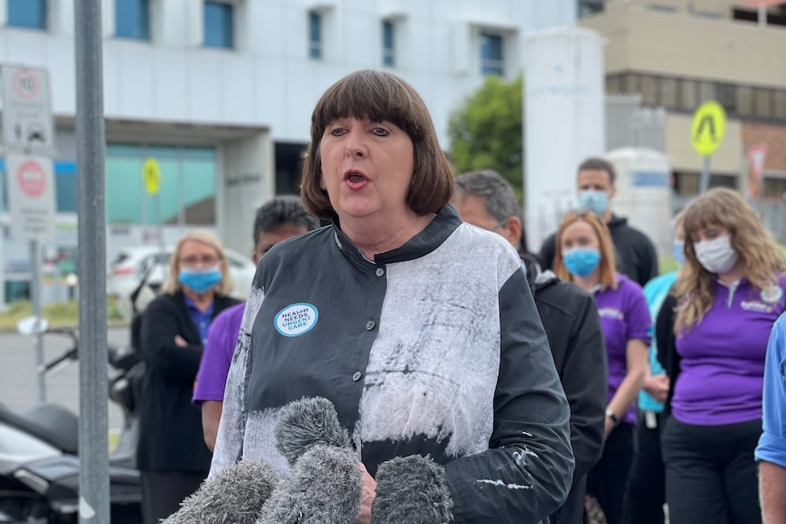 An image of Beth Mole speaking at a press conference with people behind her