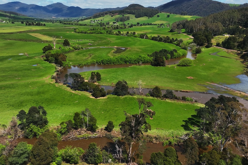 A river snakes its way through a broad green farming valley.