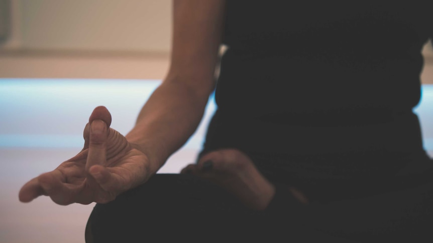 A close-up of a woman's hand in a yoga position as she sits in lotus pose.