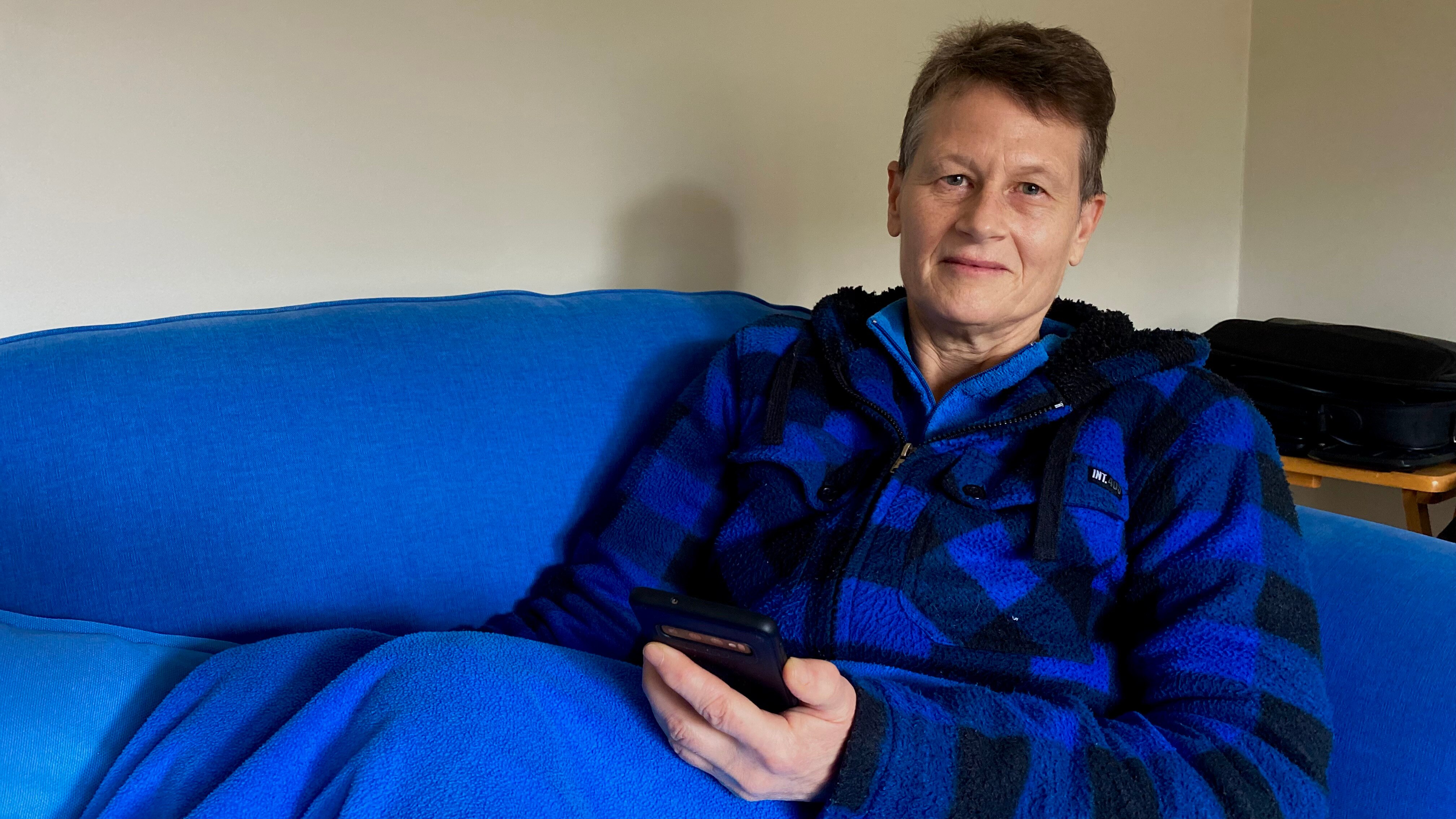 Woman in blue checked jacket sits on a blue couch
