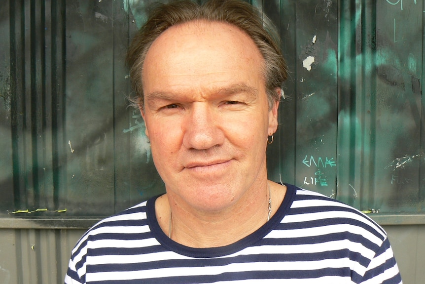A middle-aged man wearing a striped t-shirt looks seriously at the camera.