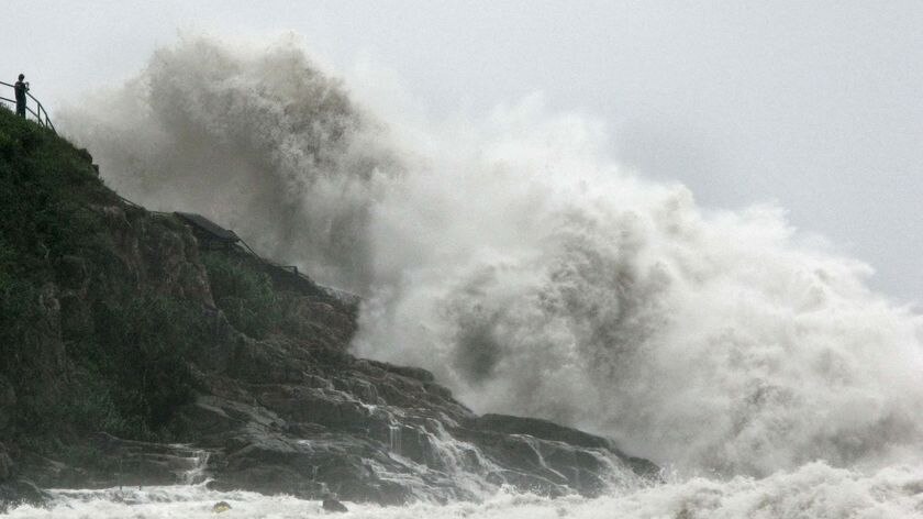 A man has a close look at waves as they crash against cliffs