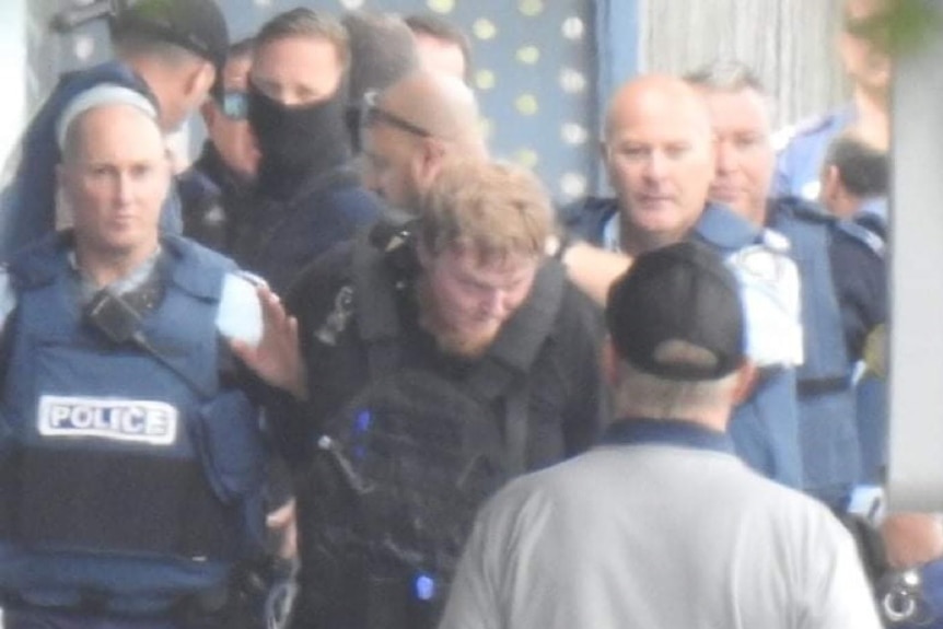 a man in black being escorted by police