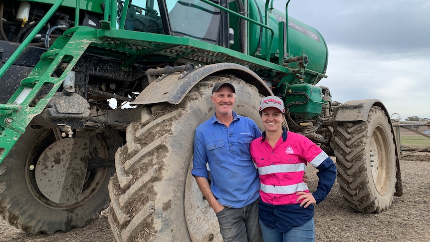 A man and a woman smiling and standing in front of a large green sprayer. 