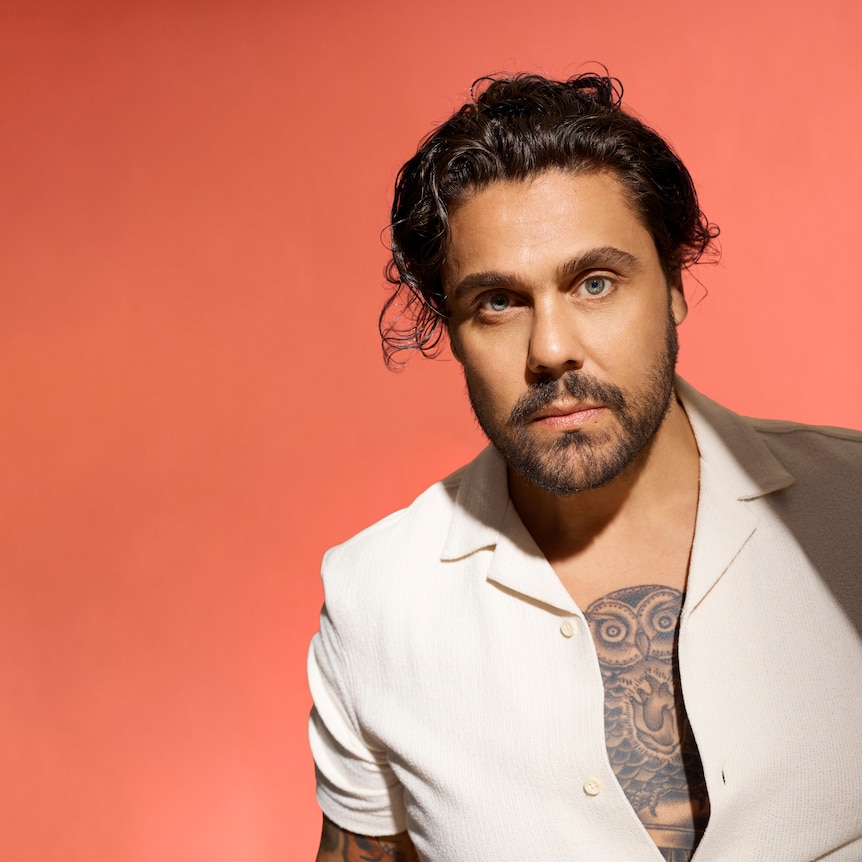 photo portrait of Dan Sultan against a burnt orange backdrop wearing an open white shirt