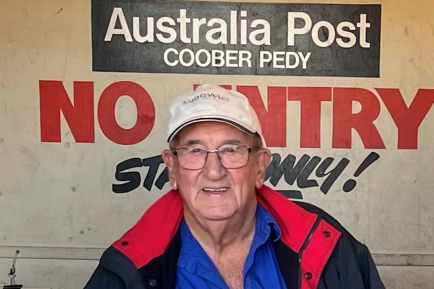 Man sits in front of Australia Post sign.