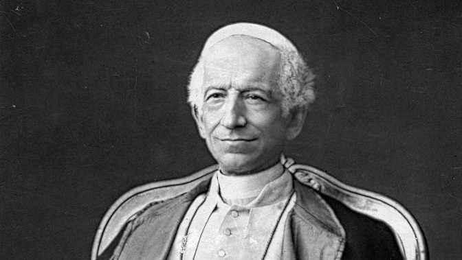 black and white portrait of older man smiling. He's wearing a pope's hat, clerical collar, religious robes and cross necklace.