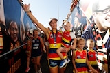 Erin Phillips walks down the race, holding a child in one arm and holding up her other hand