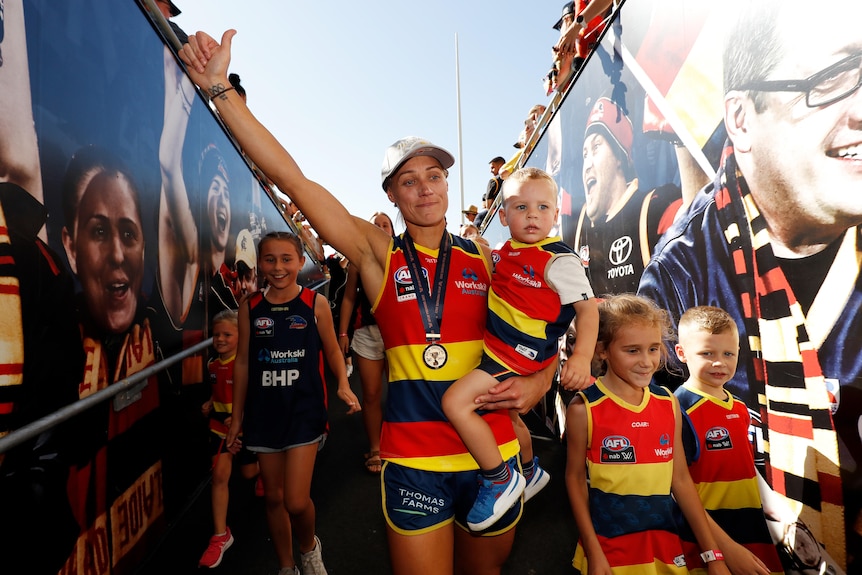 Erin Phillips walks down the race, holding a child in one arm and holding up her other hand