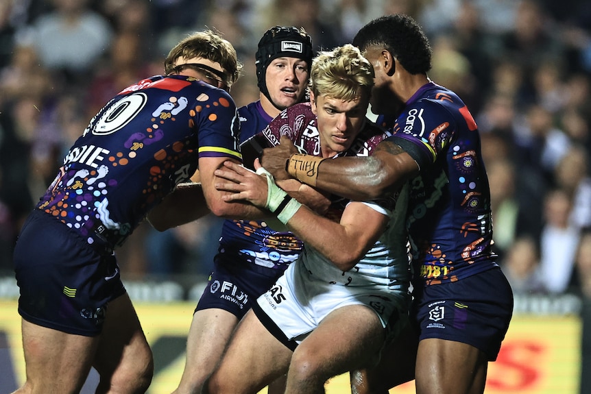 NRL player Ben Trbojevic is tackled by three opponents as he carries the football