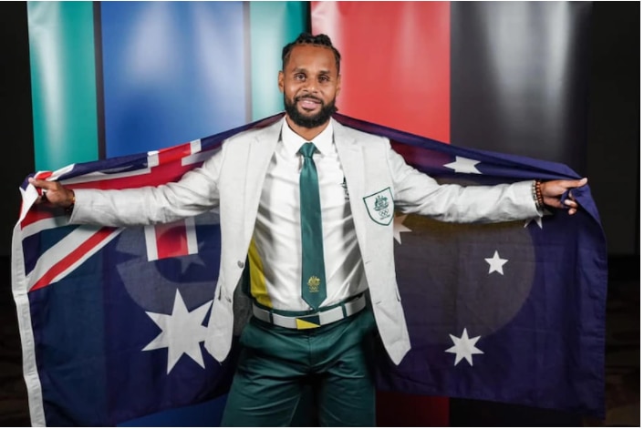 Patty Mills in his Olympic uniform holding the Australian flag 