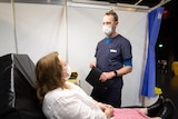 A woman wearing a face mask talking to a nurse.
