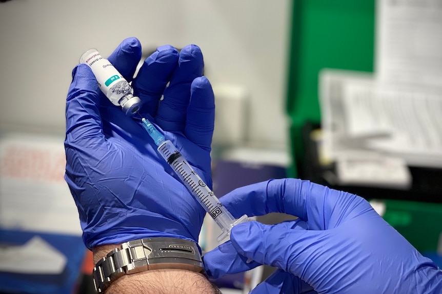 A pair of gloved hands uses a syringe to measure a vaccine.