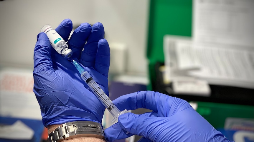 A pair of gloved hands uses a syringe to measure a vaccine.