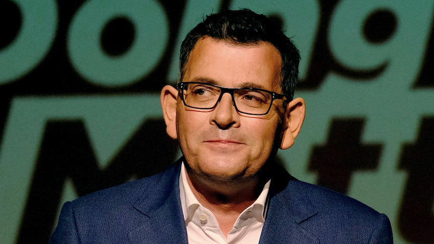 Daniel Andrews smiles, dressed in a suit delivering a speech.