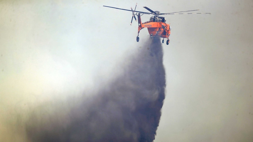 A helicopter drops water on a burning wildfire in California.