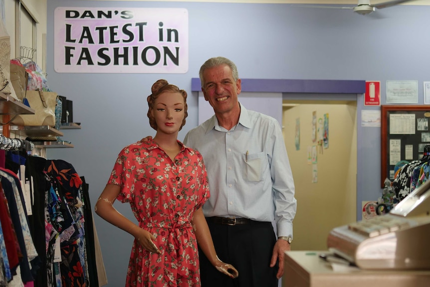 A male shopkeeper stands in a ladies clothing store, next to a mannequin