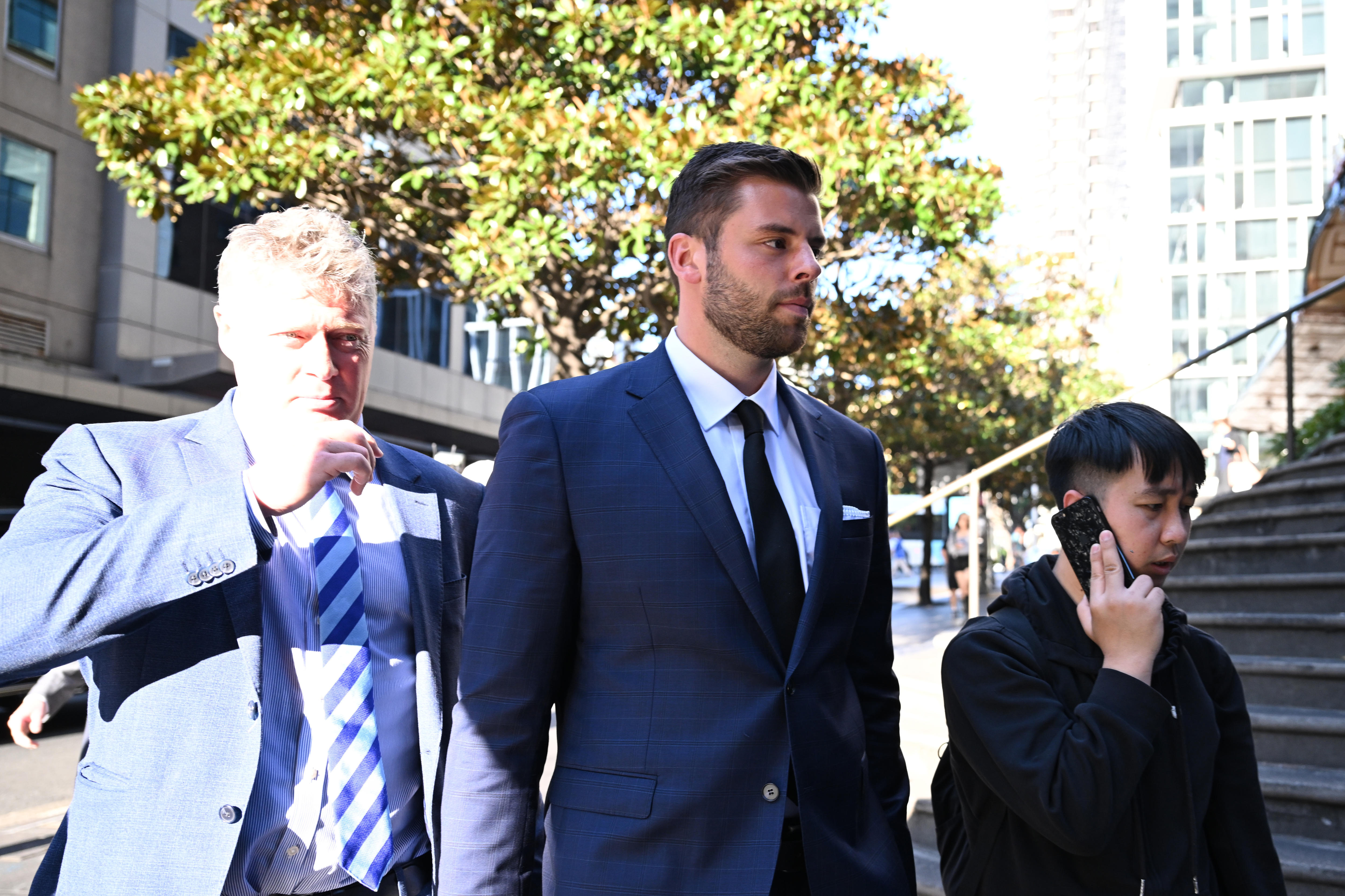 A man in a suit stares ahead outside a court house with another man in a suit next to him on his right.