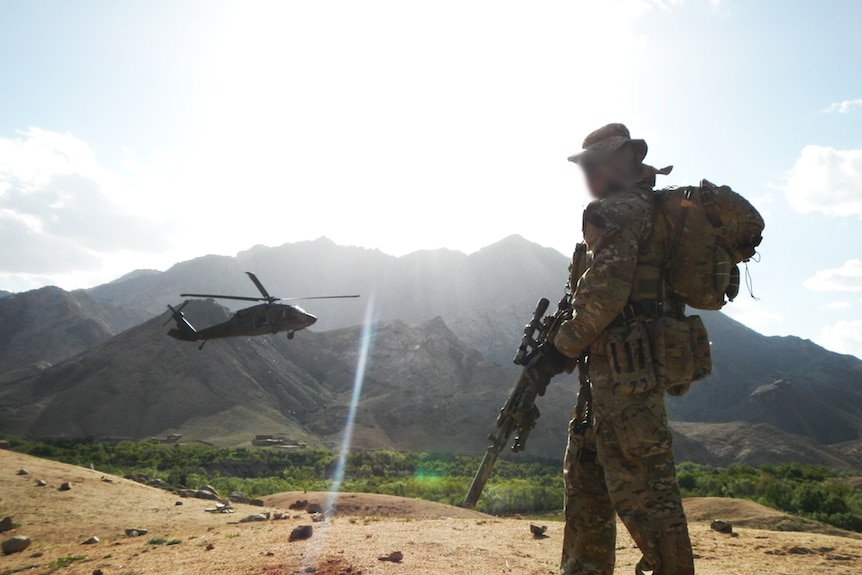 SAS soldier overlooks valley in Afghanistan as Black Hawk helicopter flies past in 2012.