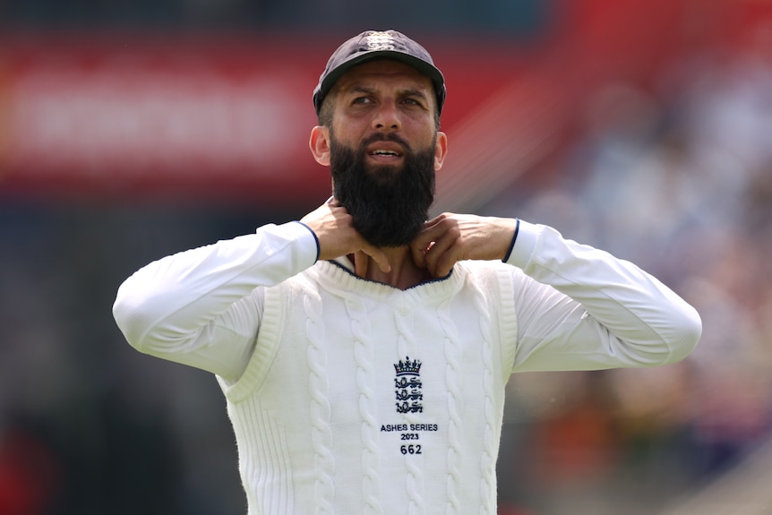 Moeen Ali looks up and holds his collar