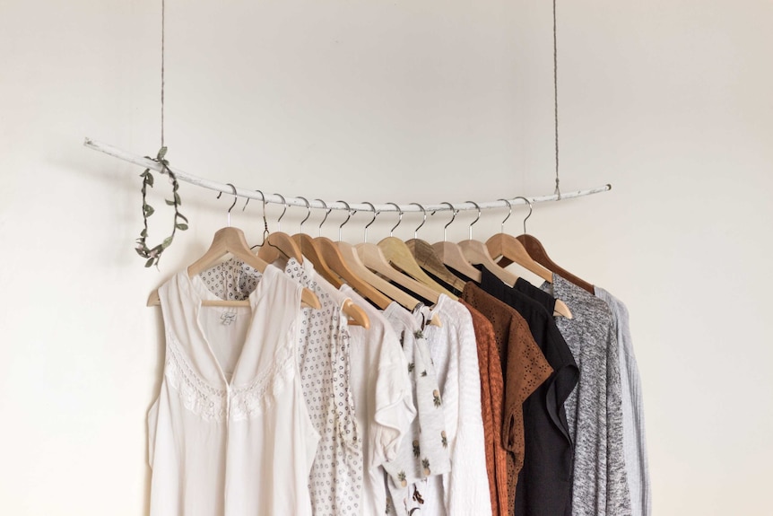 Neutral clothing hangs from a rack to depict classic style.