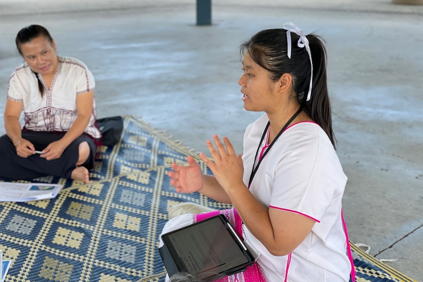 a woman sat cross legged speakinh to a group, with an ipad on her lap