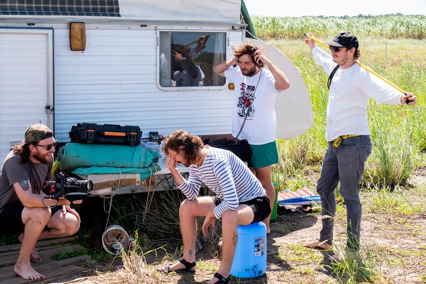 Four men, part of a film crew, stand outside beside a caravan. 