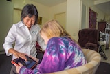 A woman with a shirt that says Care West helps an older woman with an electronic tablet