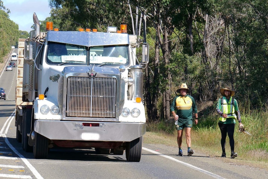 Alwyn Doolan, holding his message stick, and Peter Bartlett walk on a Yeppoon road side.