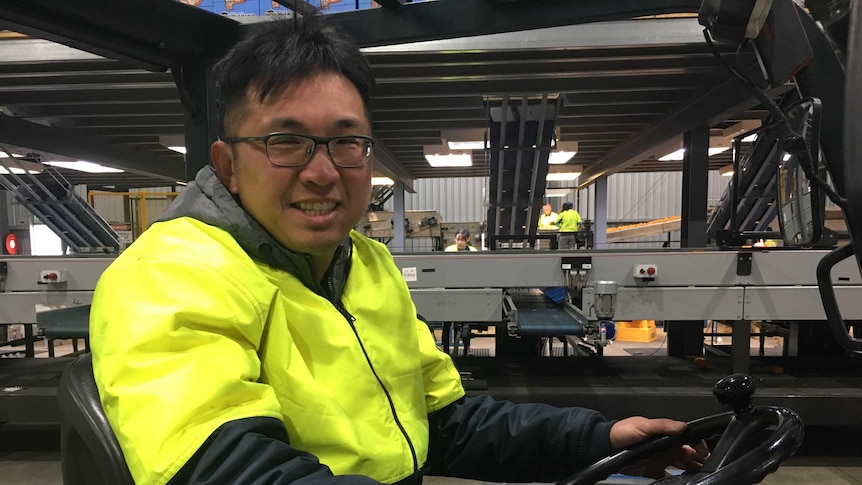 A man smiles at the camera while operating a forklift in a warehouse