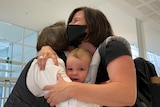 A group of people hug with a baby looking at the camera