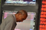Investor looks down in front of electronic board showing stock information