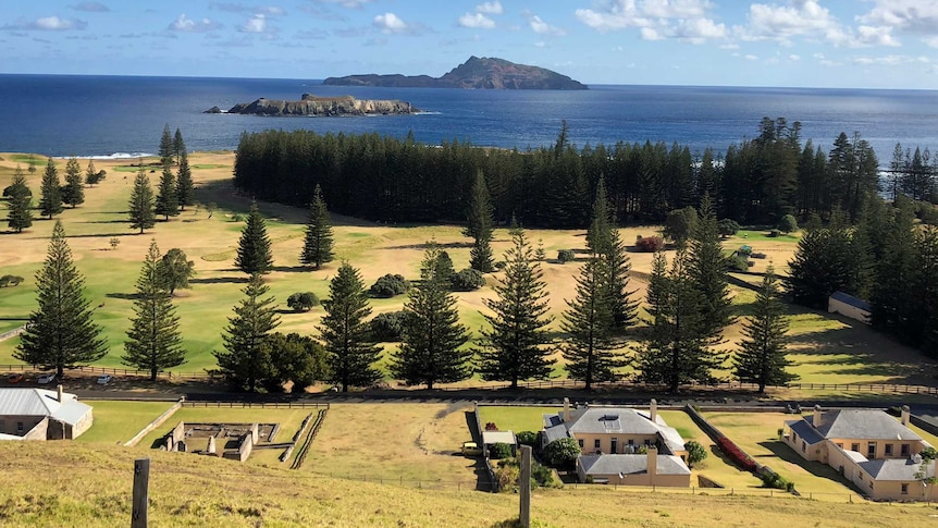 Norfolk Island looking out onto Phillip Island shows dry yellowing grass and old penal buildings
