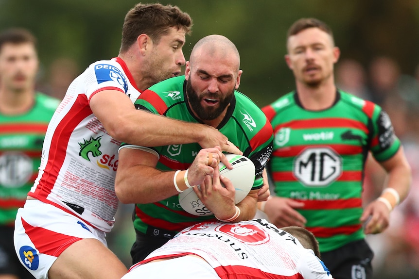 A South Sydney NRL player holds the ball as he is tackled against St George Illawarra.