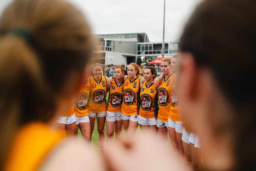 Curtin Uni Wesley players stand arm in arm in a huddle at an Aussie rules match.