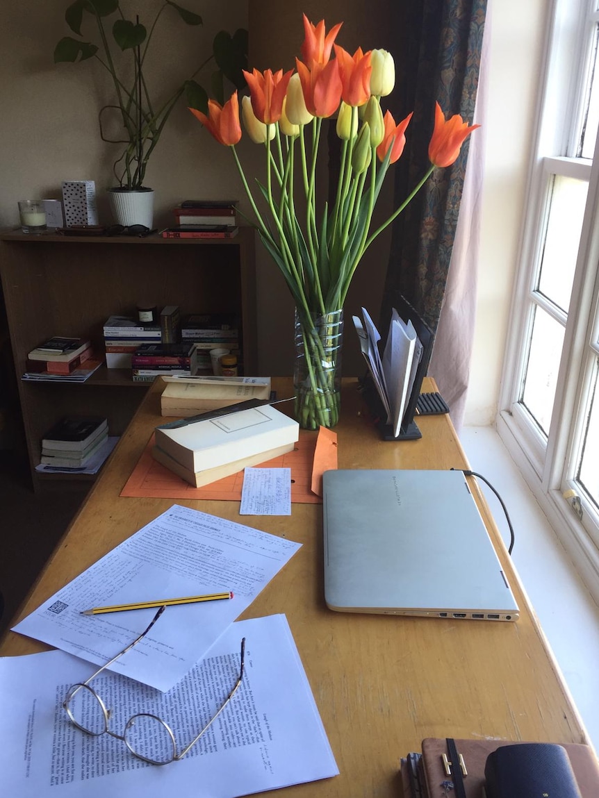 A bunch of tulips in a vase on a desk with a laptop and study papers.