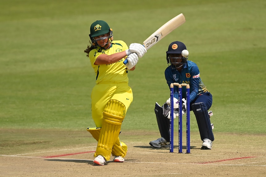 An Australian cricketer in a green and yellow uniform plays a shot as a Sri Lankan player keeps wickets
