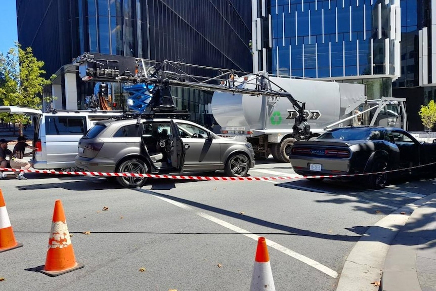 cast and crew crowd around cars on a movie set