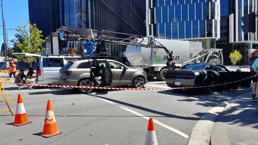 cast and crew crowd around cars on a movie set