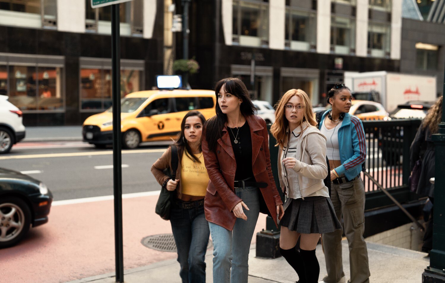 A woman and three teen girls look around them as they emerge from a subway stairwell and walk a city street.