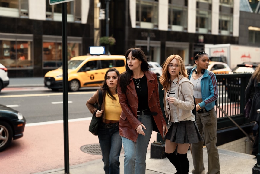 A woman and three teen girls look around them as they emerge from a subway stairwell and walk a city street.