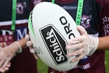 A ball boy holds an NRL rugby league ball while wearing a pair of gloves.