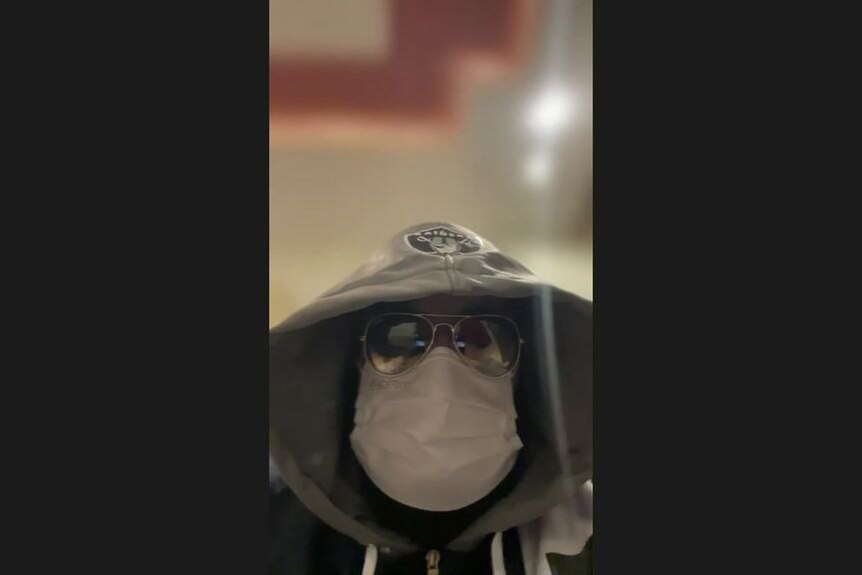 A man wearing a mask, sunglasses and hoodie.