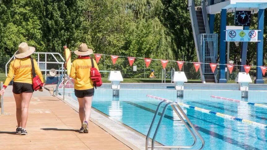 Two lifeguards walking along the edge of a public pool 