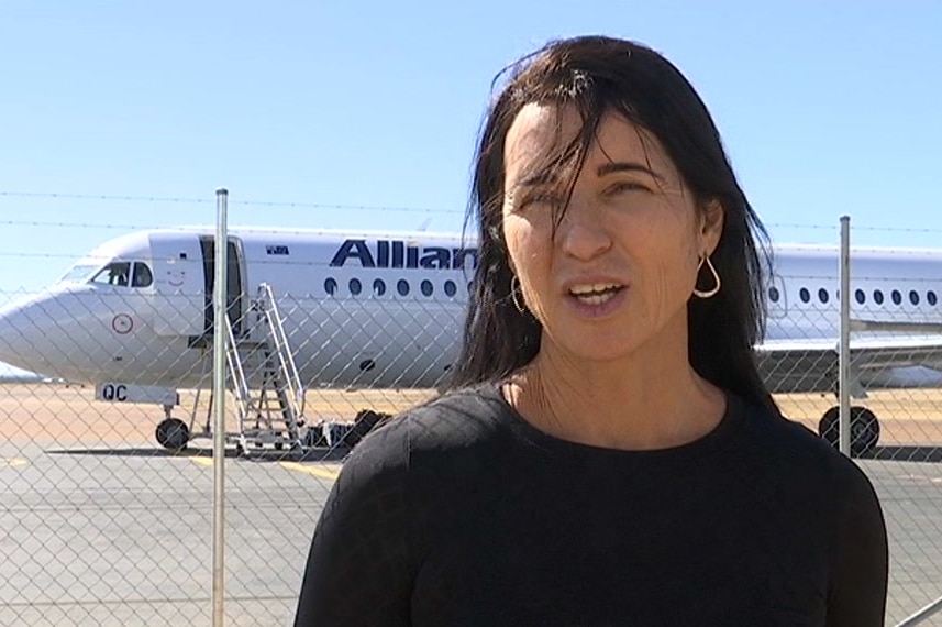 A woman standing near the apron of a regional airport, a plane in the background