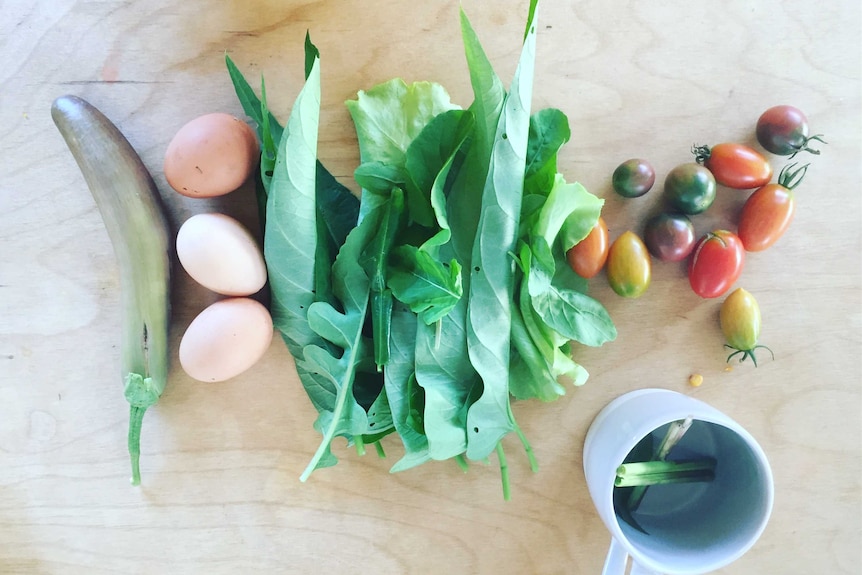 Three eggs, some salad and eggplant on a table.